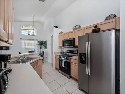 a kitchen with a stainless steel refrigerator and wooden cabinets at Oasis Key Retreat by PropertyChekker! in Kissimmee