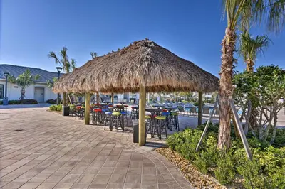 a patio with tables and chairs under a straw umbrella at Lanai and Private Pool, 8 Mi to WDW Family Getaway! in Kissimmee