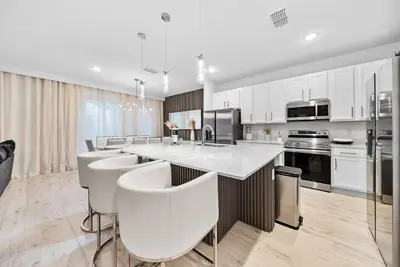 a kitchen with white cabinets and a large island with bar chairs at Dream 8-Bedroom Home with Pool in Kissimmee