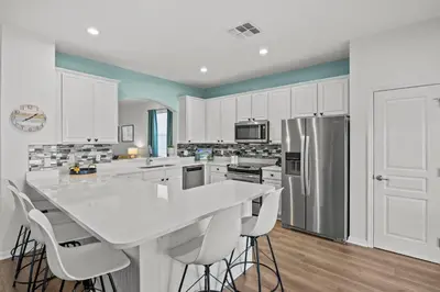 a kitchen with white cabinets and a kitchen island with stools at 6 BR Home, Themed Rooms, Private Pool, Windsor Hills by Blue Sky Villas in Orlando