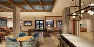 a lobby with tables and chairs and a restaurant at Staybridge Suites Orlando Universal Blvd by IHG in Orlando