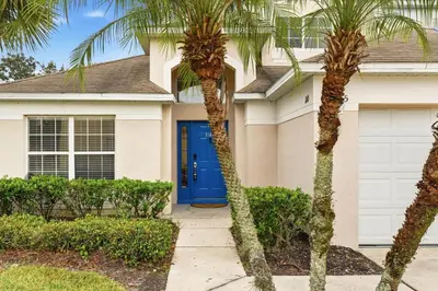 a house with a blue door and palm trees at The Seasons Retreat 5BR Oasis with Private Pool in Kissimmee