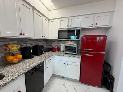 a red refrigerator in a kitchen with white cabinets at Disney Princess and Heroes Apartment Accessible in Orlando