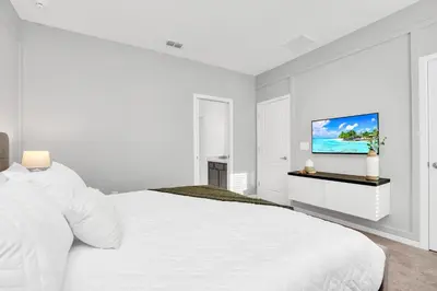 a white bedroom with a white bed and a flat screen tv at Luxurious 15-Bedroom Villa With Pool & Games Room in Kissimmee