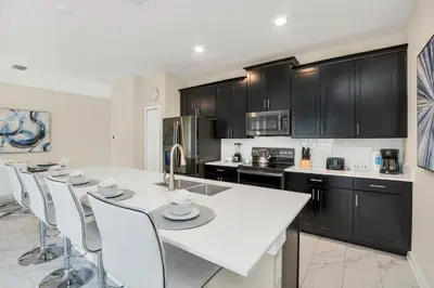 a kitchen with black cabinets and a white table and chairs at Ev2861 - Sunshine Grove Villa in Kissimmee