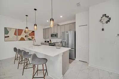 a white kitchen with a large white counter and stools at Ev4228 - Storey Retreat in Kissimmee