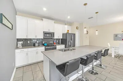 a kitchen with white cabinets and a large island with chairs at Ev4927 - Beautiful Storey Lake in Kissimmee