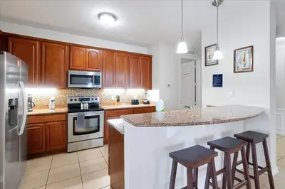 a kitchen with wooden cabinets and a island with bar stools at Beautiful Condo, Near Epic Universe and OCCC-2018 by Vista Cay Resort in Orlando