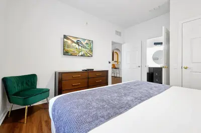 a white bedroom with a bed and a green chair at Luxury 2BR Epic Universe Condo at Vista Cay 3029 by Vista Cay Resort in Orlando