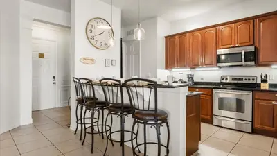 a kitchen with wooden cabinets and a counter with bar stools at Upstay Great 3BR Condo w Scenic Views & Patio in Orlando