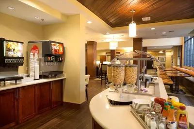 a restaurant with a counter with food and a tv at Staybridge Suites Orlando at SeaWorld by IHG - Free Breakfast & Shuttle to SeaWorld Parks in Orlando