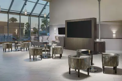 a lobby with tables and chairs and a flat screen tv at DoubleTree by Hilton Orlando Airport Hotel in Orlando