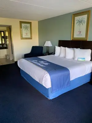 a hotel room with a large bed and a chair at Days Inn by Wyndham Orlando Airport Florida Mall in Orlando