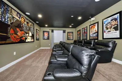 a movie room with black leather couches and posters at Vibrant Elite Home With Private Pool, Theater Room And Waterpark & Resort Access Near Disney At Encore Resort - 7605Mc in Kissimmee