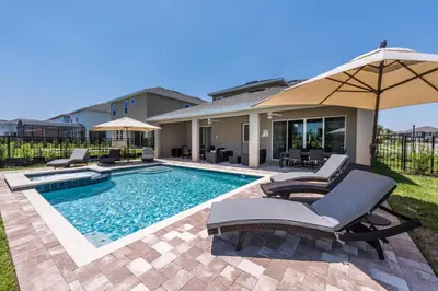 a swimming pool with chairs and an umbrella next to a house at Elegant Home Near Disney With Private Pool And Waterpark & Resort Access At Encore Resorts Reunion - 391Fl in Kissimmee