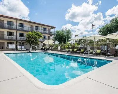 a pool with chairs and umbrellas next to a hotel at Quality Inn & Suites By the Parks in Orlando