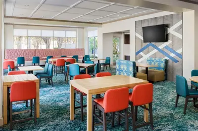 a waiting room with tables and chairs and a flat screen tv at Hilton Garden Inn Orlando at SeaWorld in Orlando