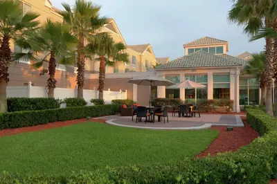 a house with palm trees and a patio with tables and umbrellas at Hilton Garden Inn Orlando East - UCF Area in Orlando