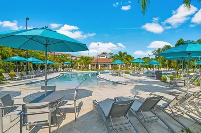 a pool with tables and chairs and blue umbrellas at Beautiful LAKEVIEW Deluxe Condo Near Theme Parks in Orlando