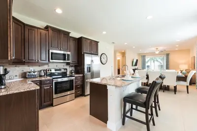 a kitchen with wooden cabinets and a kitchen island with chairs at Vibrant Home Near Disney With Private Pool, Themed Rooms And Waterpark & Resort Access At Encore Resorts Reunion - 401No in Kissimmee
