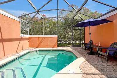 a swimming pool with an umbrella next to a table and a table at Encantada Resort Vacation Townhomes by IDILIQ in Kissimmee