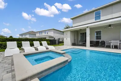 a swimming pool with white chairs and a house at Striking Home With Games, Outdoor Kitchen Near Disney With Waterpark & Resort Access At Encore Resort - 7742Ff in Kissimmee