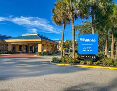 a sign in front of a building with palm trees at Hotel Monreale Express & Studios IDrive District in Orlando