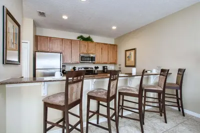 a kitchen with wooden cabinets and a bar with chairs at Paradise Palms-4 Bed Townhome W-Splashpool-3044Ppr in Kissimmee