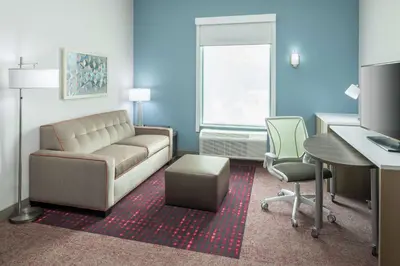 a living room with a couch and a desk and chair at Home2 Suites By Hilton Orlando Airport in Orlando