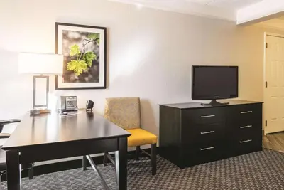 a hotel room with a desk and a tv and a chair at La Quinta by Wyndham Orlando Airport - On Property Food Trucks & Free Airport Shuttle! in Orlando