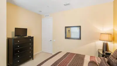 a bedroom with a bed and a dresser with a television at Merlyns Magic Condo - closer to Disney in Orlando