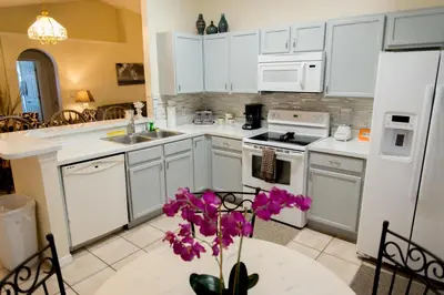 a kitchen with white cabinets and a table with purple flowers at Private Pool House With Private Pool, Near All Famous Attractions!!! in Kissimmee