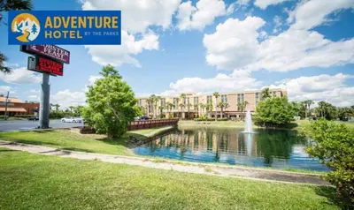 a sign for a hotel with a pond in front of a building at The Adventure Hotel by the Parks in Orlando