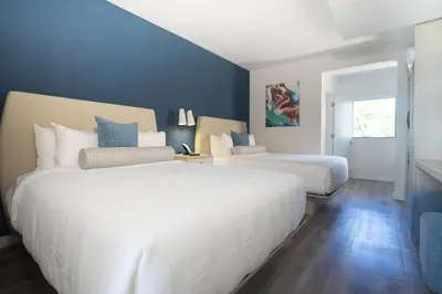 two white beds in a bedroom with blue walls at DASKK Orlando Hotel near Universal Blvd, an Ascend Collection Hotel in Orlando