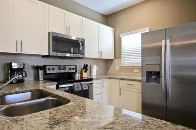 a kitchen with a stainless steel refrigerator and white cabinets at Amazing townhouse fits 10 in gated community 10 min to Disney! in Kissimmee
