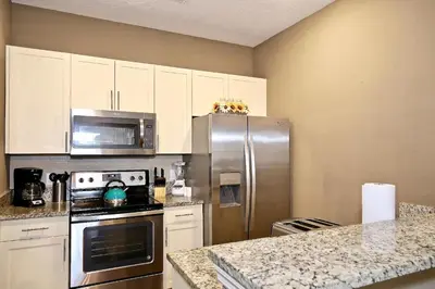 a kitchen with a stainless steel refrigerator and white cabinets at Fantastic Townhouse in Lux community sleeps 8, 10' to Disney!! in Kissimmee