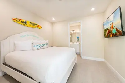 a white bedroom with a white bed and a surfboard on the wall at Livin' For The Weekend Cottage Near Disney With Margaritaville Resort & Island H2O Access - 8021Ff in Orlando
