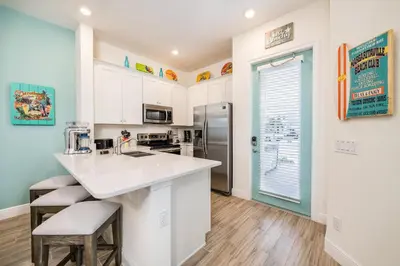 a kitchen with white cabinets and a counter with stools at Sun Baked Cottage With Hot Tub Near Disney With Margaritaville Resort & Island H2O Access - 8089Dr in Orlando