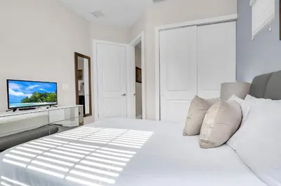 a white bedroom with a white bed and a television at 5 BR 6 BA Luxury Villa 5 min to Disneyworld Hot Tub & BBQ 112 in Orlando