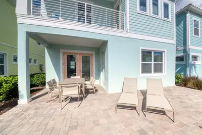 a patio with a table and chairs in front of a building at Coral Reef Cottage! Near Disney With Margaritaville Resort & Island H2O Access - 8052Ls in Orlando