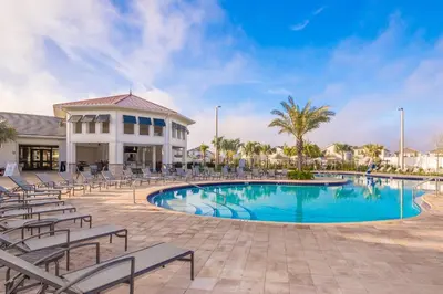 a swimming pool with chairs and a building at 4993FP TOWNHOUSE 4 BEDROOMS & 3 BATHROOMS + POOL in Kissimmee