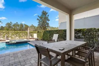 a patio with a wooden table and chairs next to a pool at 551 Villa 8BD PoolSpa - Game room Movie room in Orlando