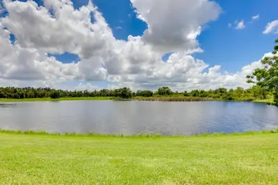 a large pond with a green field and clouds at Steps to Pool Winter Garden House with Lanai! in Orlando