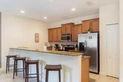 a kitchen with a refrigerator and some bar stools at Townhome w pool near Disney & Orlando Attractions in Kissimmee