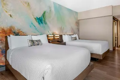two beds in a room with a painting on the wall at Cambria Hotel Orlando Airport in Orlando