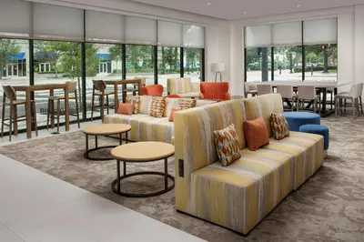 a living room with couches and tables and windows at Hilton Garden Inn Orlando Downtown in Orlando