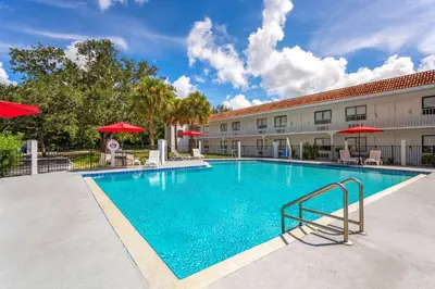 a swimming pool in front of a hotel with red umbrellas at Travelodge by Wyndham Orlando Lake Buena Vista South in Kissimmee