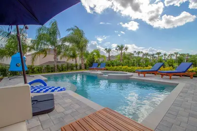 a swimming pool with blue chairs and an umbrella at Encore Resort 6 Bedroom Vacation Home with Pool (2102) in Orlando