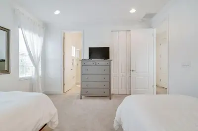 a white bedroom with two beds and a television at Beautiful Home Near Disney with Private Pool! villa in Orlando