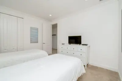 a white bedroom with two beds and a tv at Beautiful Home Near Disney with Private Pool! villa in Orlando
